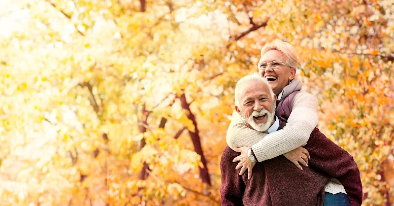 Pareja feliz en otoño en argaluza residencia de ancianos, pareja mayor abrazándose y riendo entre árboles de hojas doradas
