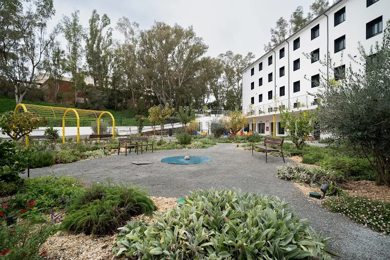 Jardín con bancos, fuente y senderos junto al edificio en clecevitam mirador del odiel residencia de mayores