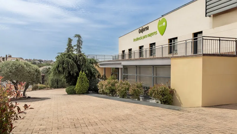 Fachada exterior y entrada pavimentada de domusvi quijorna con jardinería y terraza