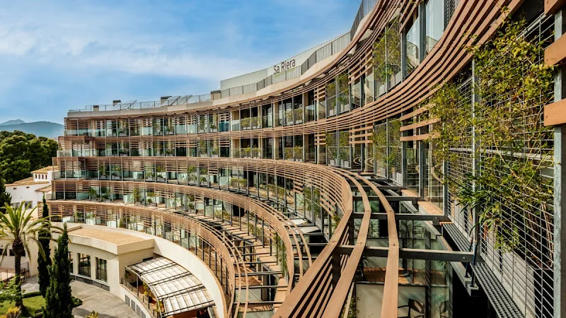 Fachada curva con balcones y vegetación de domusvi sa riera en edificio residencial moderno.