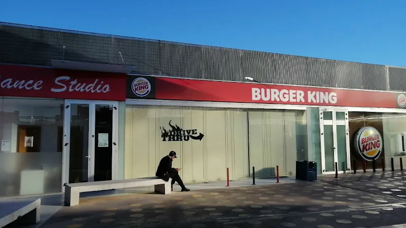 Fachada de Burger King con una persona sentada en un banco y letrero visible, geroinnova miramadrid