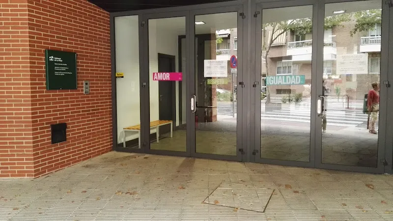 Entrada con puertas de vidrio, banco interior y carteles 'AMOR' e 'IGUALDAD' del hogar de personas mayores lobete