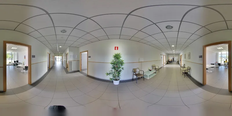 Pasillo amplio y luminoso de centro sanitario con sillas, planta decorativa y puertas a ambos lados, matia argixao