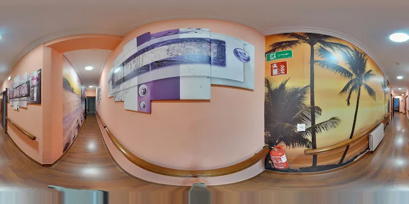 Pasillo interior decorado de la residencia ansola con mural de palmeras, barandillas y señalización de emergencia
