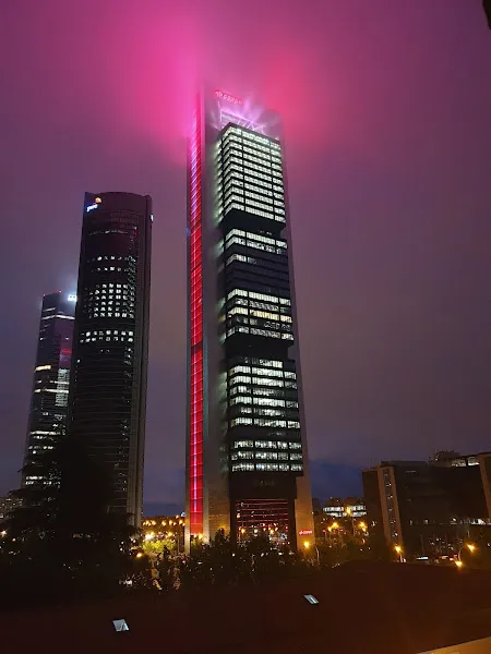 Torre moderna alta iluminada en tonos rosa y rojo con niebla en la cima, ideal para ilustrar residencia de jesus nazareno y los dolores