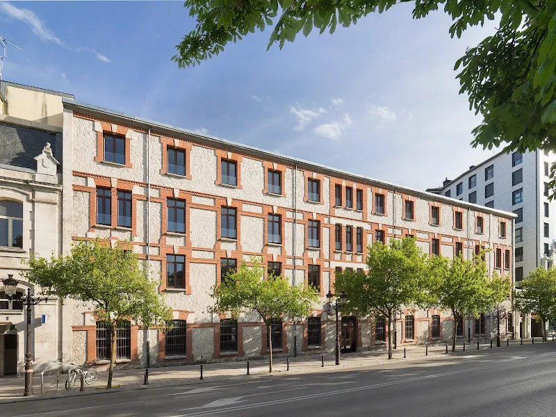 Fachada exterior soleada de la residencia de mayores clecevitam san pedro poveda con árboles y acera frente al edificio.