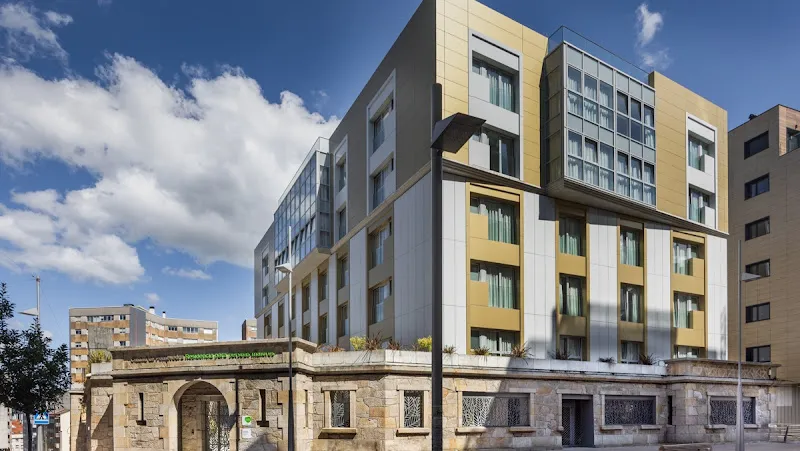 Fachada moderna y luminosa de la residencia domusvi ciudad de pontevedra con base de piedra y paneles dorados