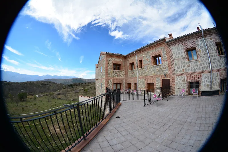 Fachada de piedra y amplia terraza con barandilla y sillas en la residencia el cerrillo frente a un valle montañoso
