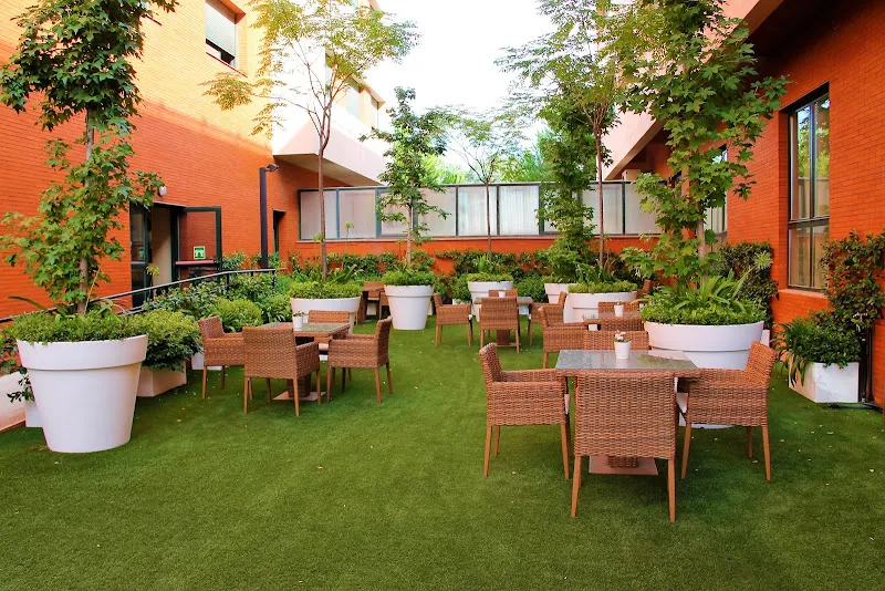 Terraza exterior con césped, mesas y maceteros en residencia para mayores ballesol alcala de henares