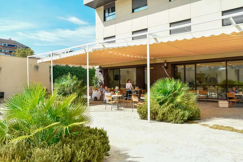Terraza exterior con mesas y personas mayores en residencia para mayores ballesol almogavares.