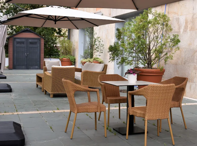 Terraza exterior con mesas, sillas de mimbre, sombrillas y macetas en residencia para mayores ballesol poio