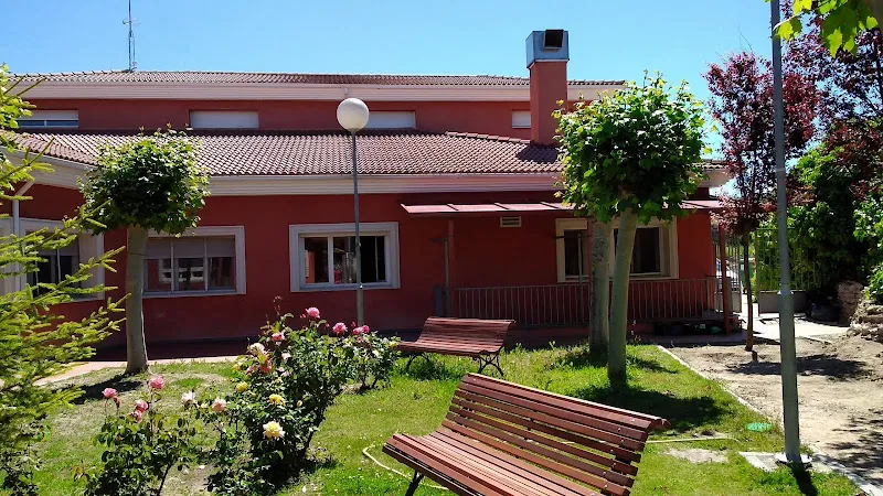 Fachada rojiza y jardín con bancos y flores de la residencia sacramenia bajo cielo despejado