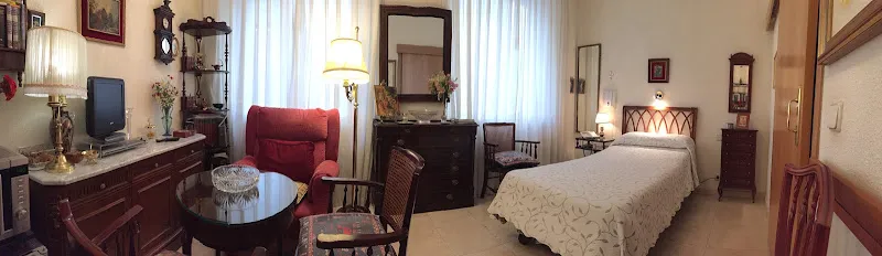 Habitación clásica y luminosa en residencia santa maria del monte carmelo pp carmelitas con cama individual, sillón y muebles antiguos.