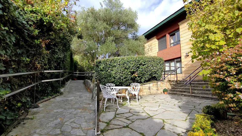 Patio exterior con mesa y sillas blancas, rampas de acceso y vegetación en residencia satistegui