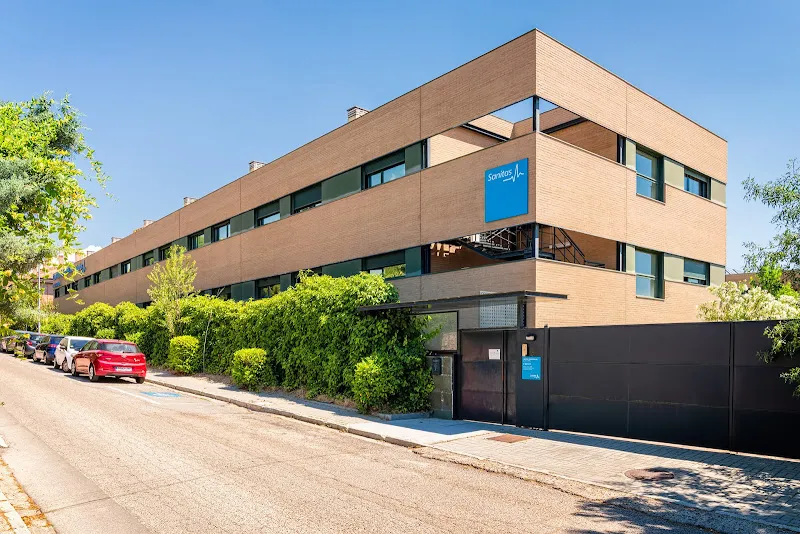 Edificio de ladrillo con rótulo azul de Sanitas en la fachada y entrada principal, sanitas residencia de mayores el escorial